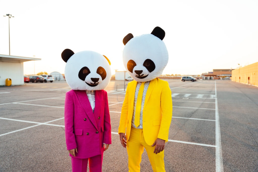 Storytelling image of a couple wearing giant panda head and colored suits. Man and woman making party in a parking lot.
